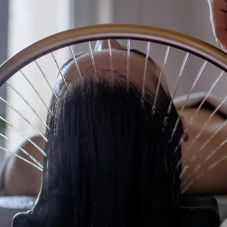 Close-up of a woman receiving a head massage during a Japanese head spa treatment with water flowing from a special hair washing tool, focusing on the scalp relaxation and beauty therapy